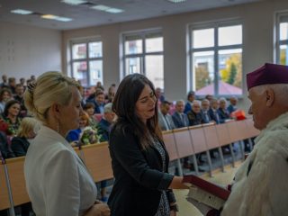 Kobieta w ciemnej marynarce odbiera gratulacje od rektora podczas wręczania wyróżnień.