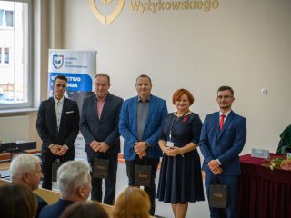 Czterej mężczyźni i kobieta pozują z upominkami przed publicznością inauguracji.