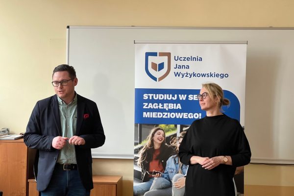 Dwoje przedstawicieli UJW prowadzi spotkanie przy tablicy i roll-upie uczelni.