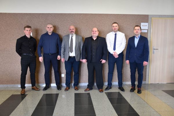 Sześciu mężczyzn pozuje w holu uczelni podczas obron na kierunku logistyka.