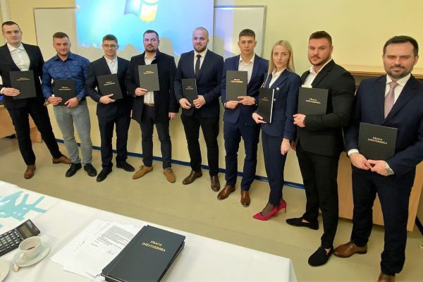 Absolwenci i członkowie komisji pozują z pracami dyplomowymi w sali UJW.