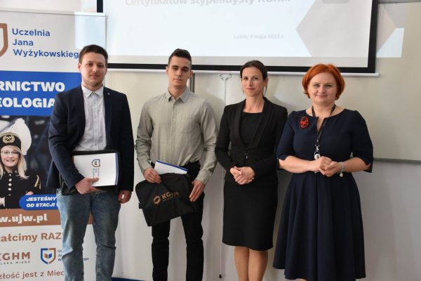 Cztery osoby pozują z dokumentami i upominkiem KGHM podczas uroczystości w UJW.