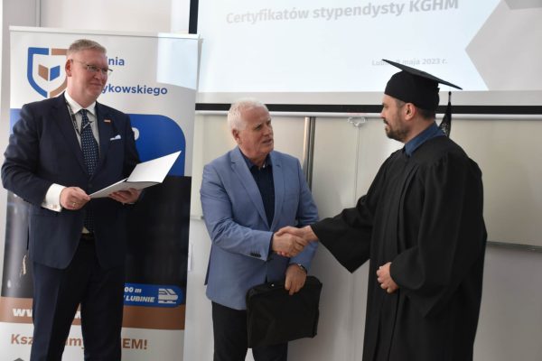 Gratulacje i uścisk dłoni podczas wręczenia dokumentu absolwentowi w todze i birecie.