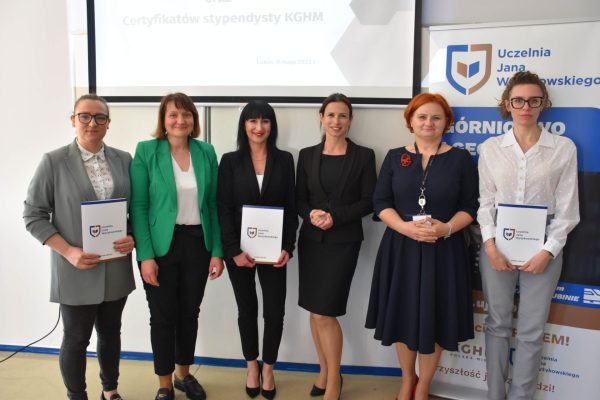 Grupa uczestników uroczystości prezentuje dyplomy na tle planszy UJW.