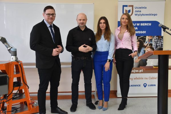 Cztery osoby pozują obok ramienia robota podczas Dnia Robotyki.