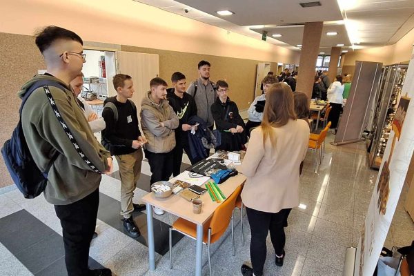 Odwiedzający rozmawiają z prowadzącą przy stoliku z materiałami w holu UJW.