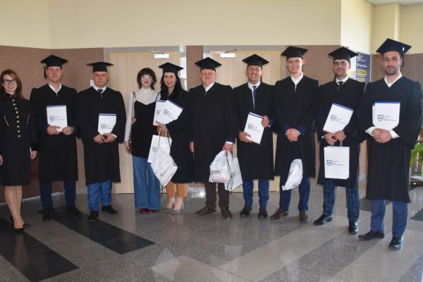 Grupa absolwentów w togach i biretach prezentuje dyplomy w holu uczelni.
