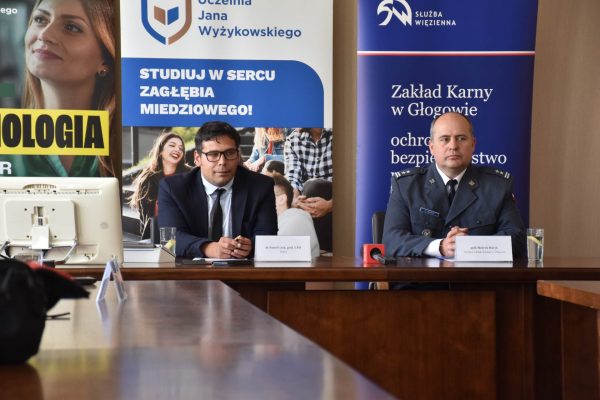 Przedstawiciele UJW i Zakładu Karnego w Głogowie przy stole na tle plansz obu instytucji.