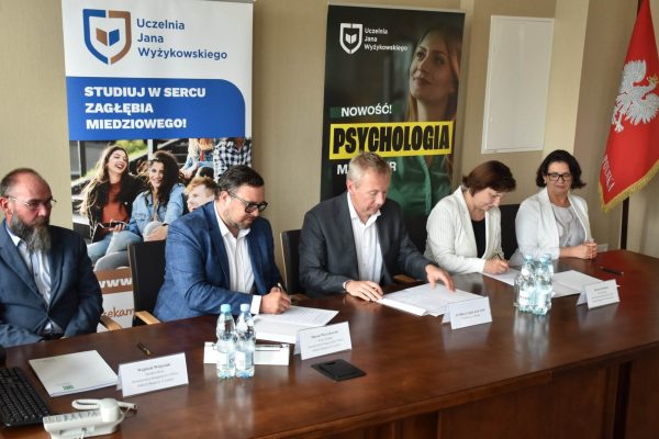 Przedstawiciele uczelni i partnera podpisują dokumenty przy stole konferencyjnym.