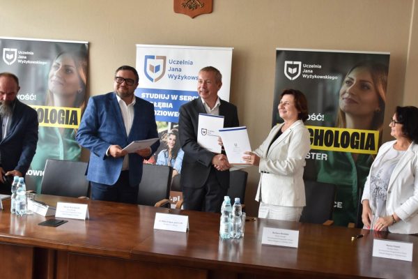 Uczestnicy spotkania stoją za stołem i prezentują dokumenty porozumienia partnerskiego.