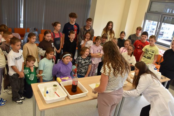 Dzieci obserwują pokaz doświadczeń przy stole z naczyniami podczas Festiwalu Nauki.