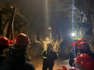 Uczestnicy terenowego projektu inżynierskiego w czerwonych kaskach zwiedzają oświetlony podziemny korytarz.