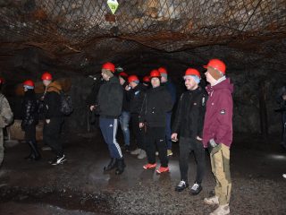 Uczestnicy terenowego projektu inżynierskiego w czerwonych kaskach stoją pod skalnym stropem zabezpieczonym siatką.