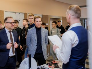 Prowadzący prezentuje materiały osobom zgromadzonym przy stoisku podczas Dnia Drzwi Otwartych.
