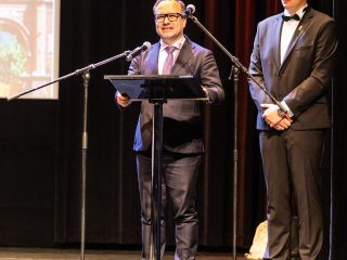 Mężczyzna przemawia przy mównicy na scenie podczas zakończenia roku szkolnego.