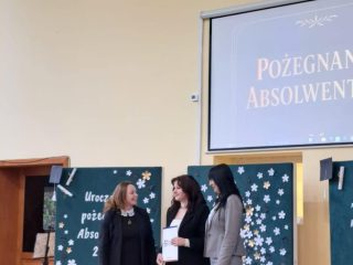 Wręczenie upominku podczas pożegnania absolwentów w szkolnej sali.