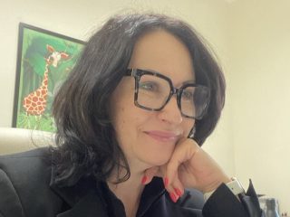 Uczestniczka konferencji w okularach siedzi przy biurku, podpierając głowę dłonią.
