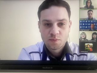 Ekran wideokonferencji z wypowiadającym się mężczyzną i miniaturami pozostałych uczestników.