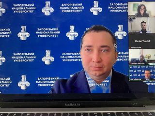 Prelegent wideokonferencji na tle planszy z logo Zaporoskiego Uniwersytetu Narodowego.
