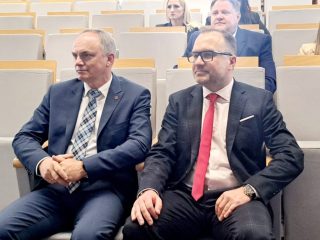 Dwaj mężczyźni w garniturach siedzą w pierwszym rzędzie podczas konferencji studenckiej.