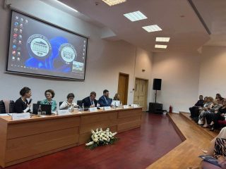 Panel konferencyjny przy długim stole przed publicznością w auli.