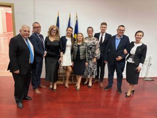 Grupa uczestników międzynarodowej konferencji pozuje w sali przy flagach.