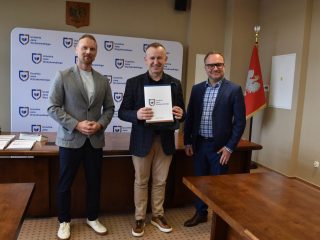 Wyróżniony w ciemnej marynarce i jasnych spodniach prezentuje certyfikat KGHM pomiędzy wręczającymi.