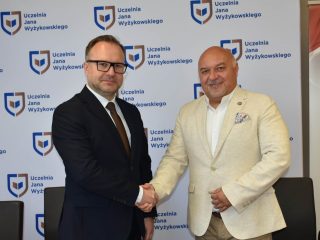 Uścisk dłoni sygnatariuszy na tle logo UJW po podpisaniu umowy.