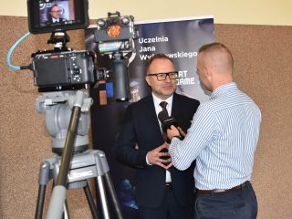 Wywiad przed kamerą z przedstawicielem UJW w ciemnym garniturze.