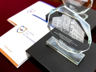 Szklana statuetka z wizerunkiem budynku UJW obok dokumentów z logo uczelni.