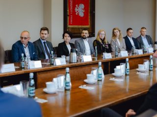 Członkowie Konwentu siedzą przy stole pod sztandarem z godłem Polski.