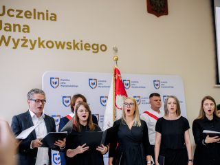 Chór śpiewa z partyturami podczas inauguracji, przy poczcie sztandarowym UJW.