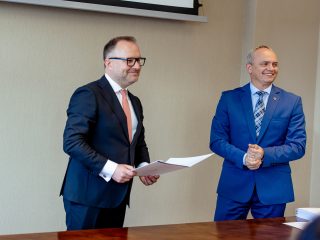 Dwaj mężczyźni stoją z dokumentami podczas spotkania Konwentu UJW.