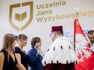 Rektor w todze i gronostajowym płaszczu stoi przed uczestniczkami ślubowania.