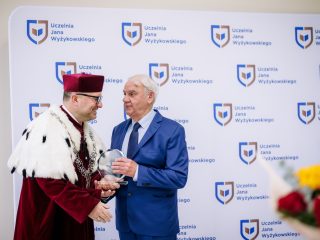 Rektor przekazuje szklaną statuetkę mężczyźnie w niebieskim garniturze.