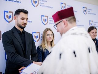 Rektor wręcza dokument mężczyźnie w czarnym garniturze.
