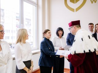 Rektor przekazuje dokument kobiecie w granatowym garniturze.