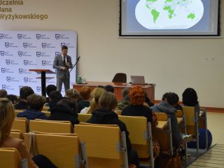 Widok z widowni na wykład z mapą świata na ekranie.