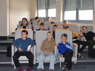 Uczestnicy festiwalu nauki siedzą w rzędach przy oknach sali wykładowej.