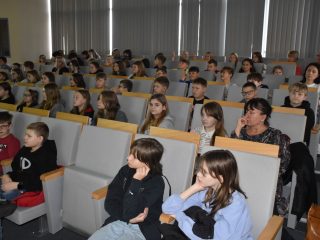 Uczniowie słuchają wykładu w sali z szarymi fotelami.