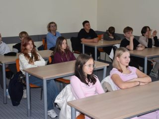 Grupa uczniów słucha prowadzącego w sali ćwiczeniowej UJW.