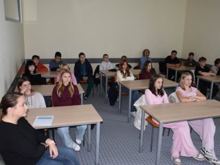 Uczniowie i opiekunowie siedzą przy ławkach podczas zajęć festiwalowych.