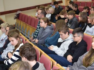 Uczniowie siedzą w czerwonych fotelach auli podczas festiwalu nauki.