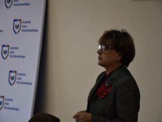 Prelegentka w okularach i szarej marynarce podczas wystąpienia na festiwalu nauki.