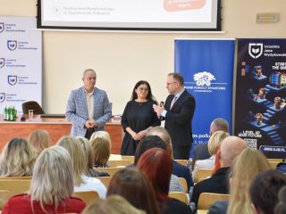 Troje przedstawicieli organizatorów stoi przed publicznością konferencji „Pomoc daje moc!”.