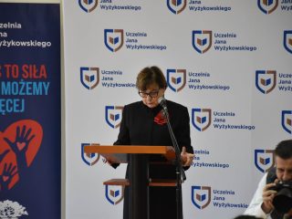 Kobieta w okularach odczytuje tekst przy mównicy na tle logo UJW.