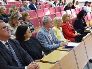 Uczestnicy konferencji siedzą przy pulpitach w rzędach auli.