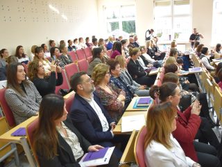 Publiczność konferencji „Pomoc daje moc!” w rzędach auli; część osób robi notatki.