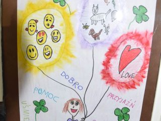 Dziecięca praca „Kocham świat” z sercem, uśmiechniętymi buziami i hasłami dobro, pomoc, przyjaźń.