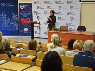 Prelegentka gestykuluje, zwracając się do uczestników konferencji OPS.